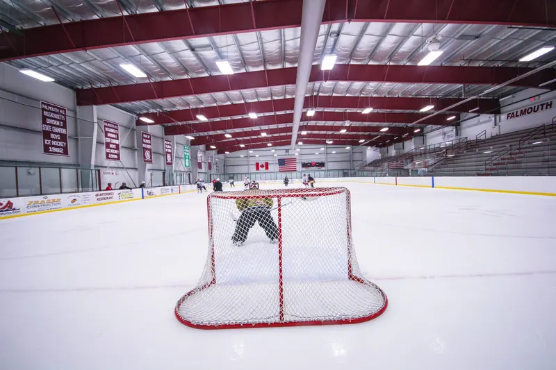 Hockey goal in front of white dasherboards and glass at the end of an indoor rink