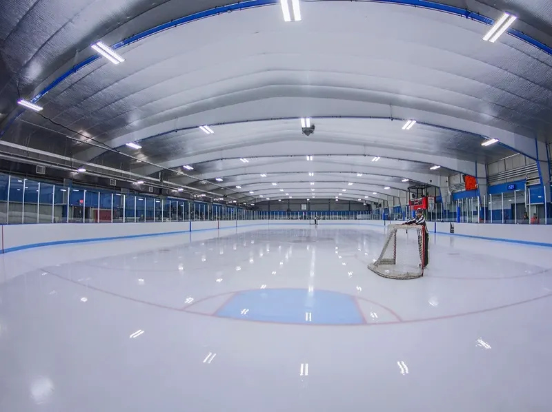 Wide view of an empty community ice arena with a resurfacer parked at the far end