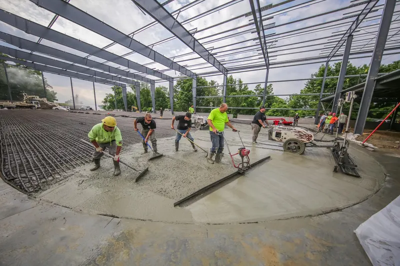Crew placing and screeding concrete over a rink floor piping grid