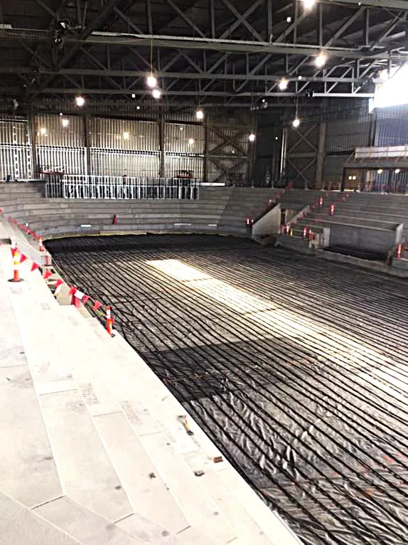 Rink floor piping runs laid out inside a steel-framed arena under construction