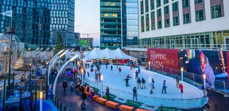 Outdoor portable ice rink busy with skaters in a downtown plaza surrounded by office towers